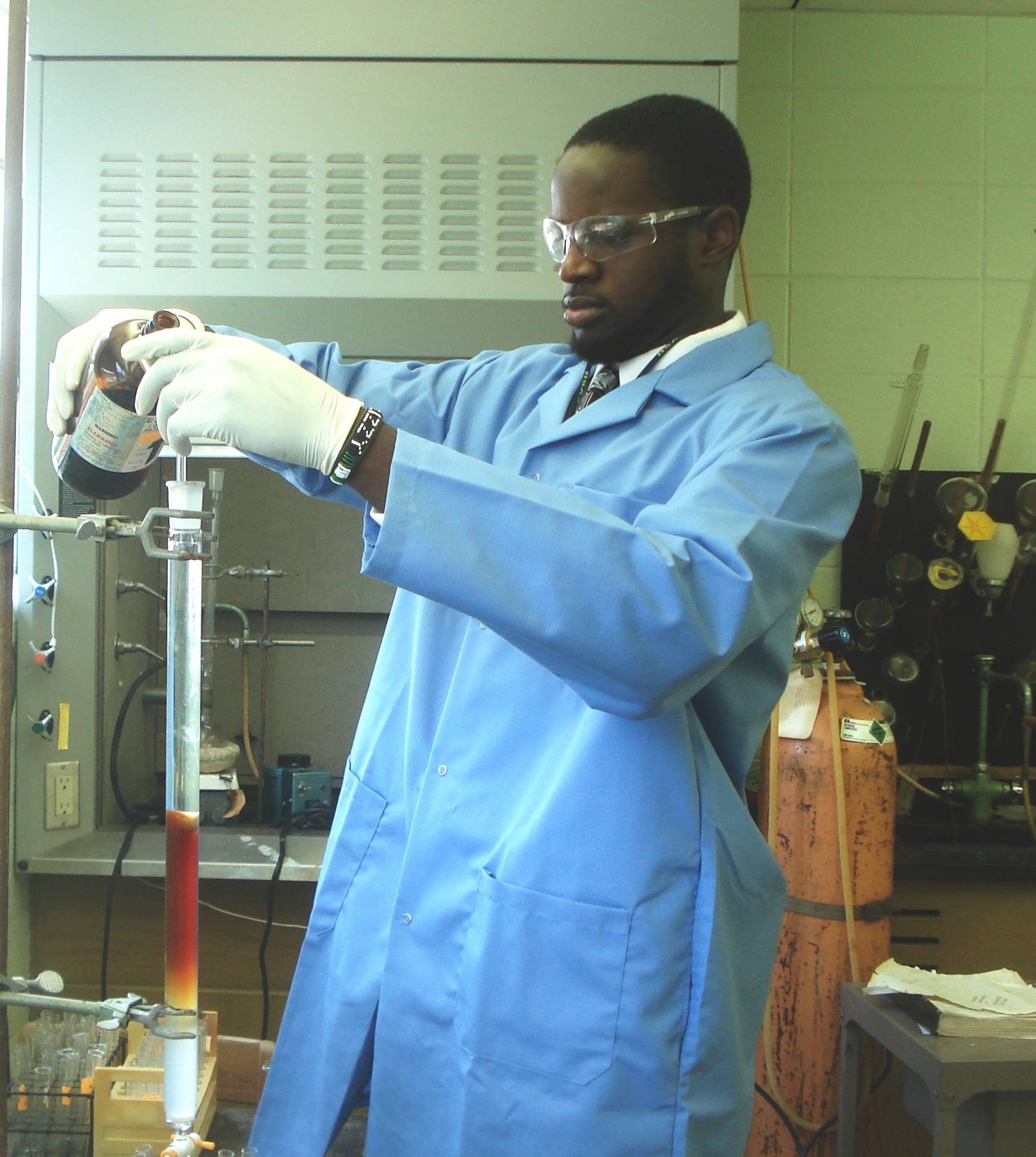 Man in blue labcoat pouring a container into a beaker